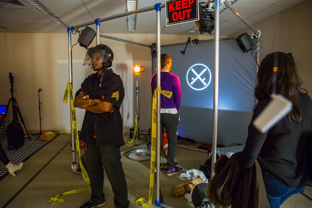 A visitor explores the RIOT installation, a large screen guarded by a man in riot gear